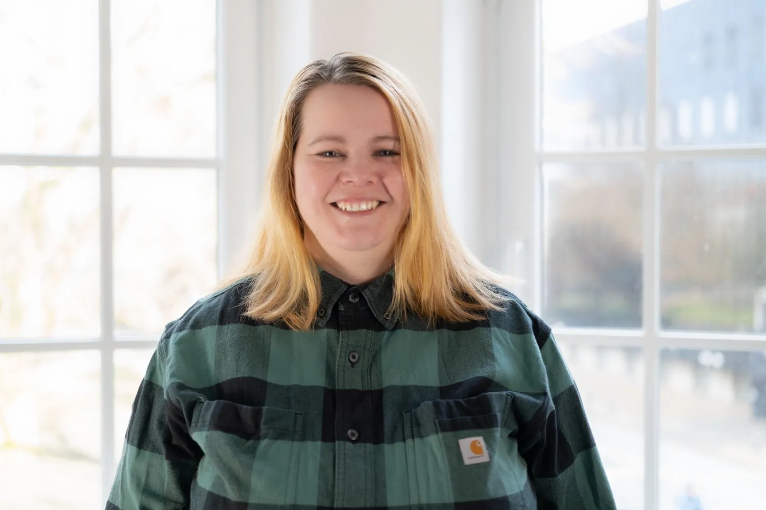 Johanna Reihs schaut freundlich in die Kamera. Sie trägt schulterlange blonde Haare und eine schwarz-grün kariertes Hemd.